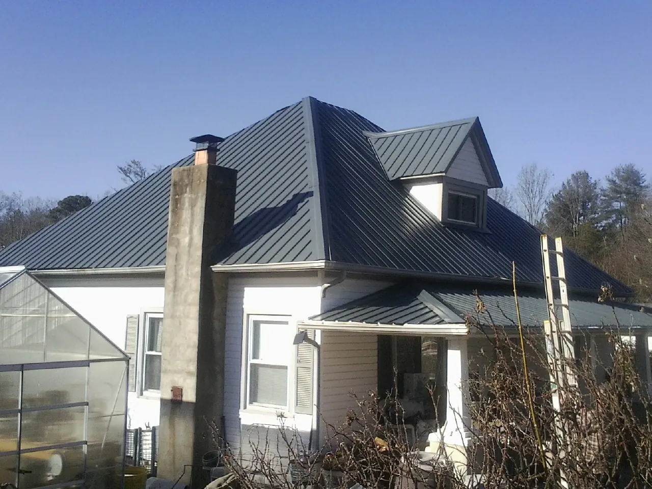 Dark blue standing seam metal roof on a white farmhouse with dormer — Slate & Tile Roof Repair by Roofing Brothers in Vining