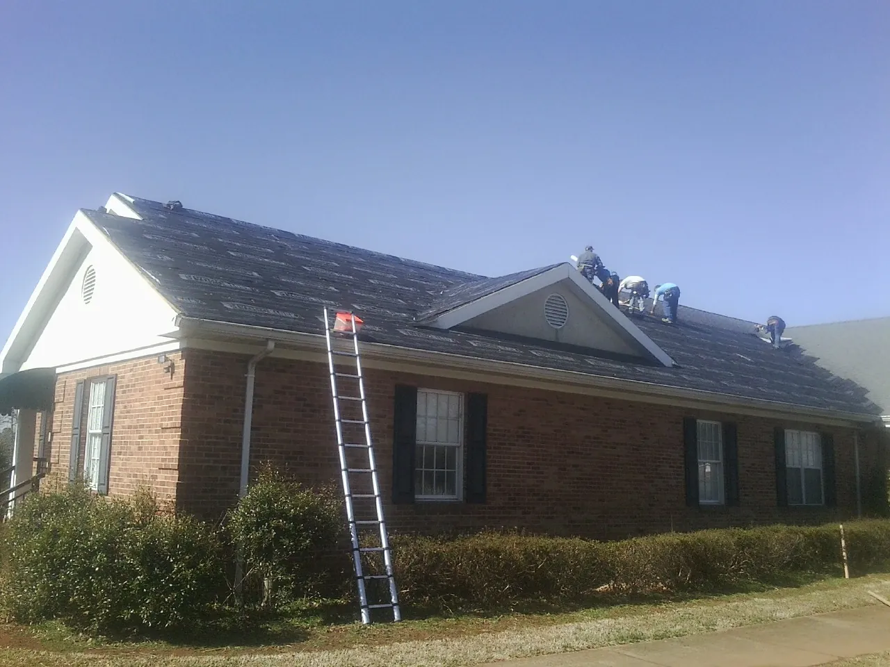 Crew tearing shingles off a brick ranch roof with a ladder set — Emergency Roof Repair work by our crew in Vining