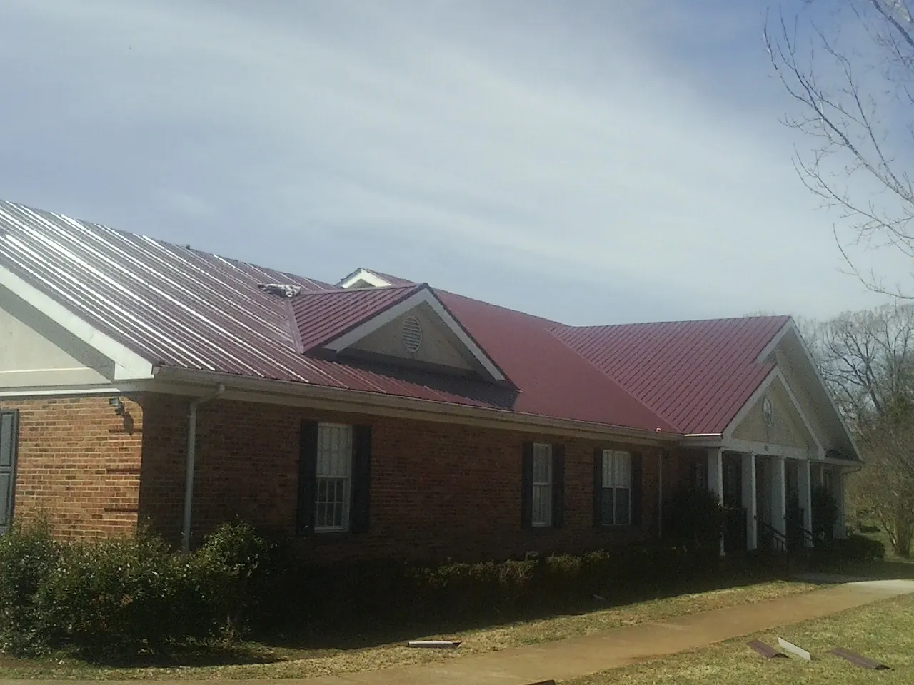 Red metal roof with gabled entries on a long brick building, from a Hail Damage Roof Repair job in Vining
