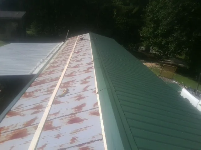 Old rusted panels beside newly installed green metal roofing — Wind Damage Roof Repair by Roofing Brothers in Vining