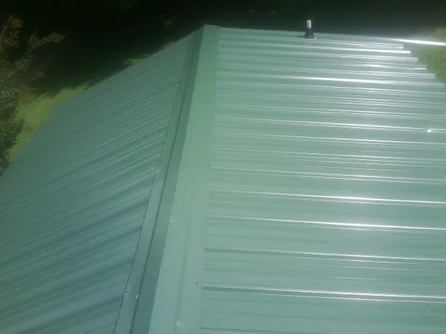 New green metal panels meeting at the ridge of a roof — Flat Roof Repair work by our crew in Vining
