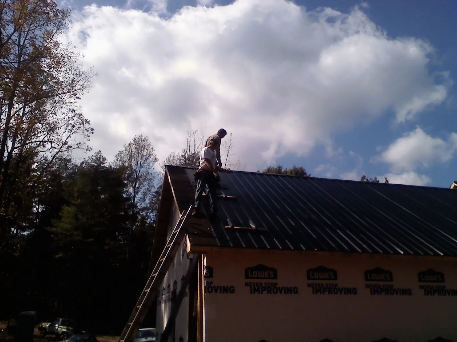 Roofer fastening dark metal panels high against a cloudy sky, from a Roof Inspection job in Vining